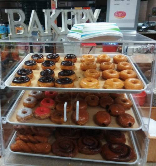 A display case filled with various donuts, including glazed, chocolate-covered, and a few with sprinkles.