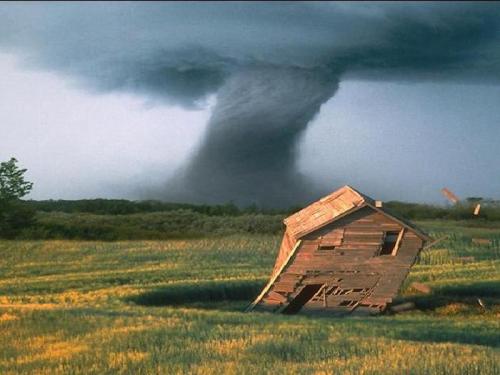 A tornado looms over a tilted, abandoned house in a grassy field, with dark storm clouds above.