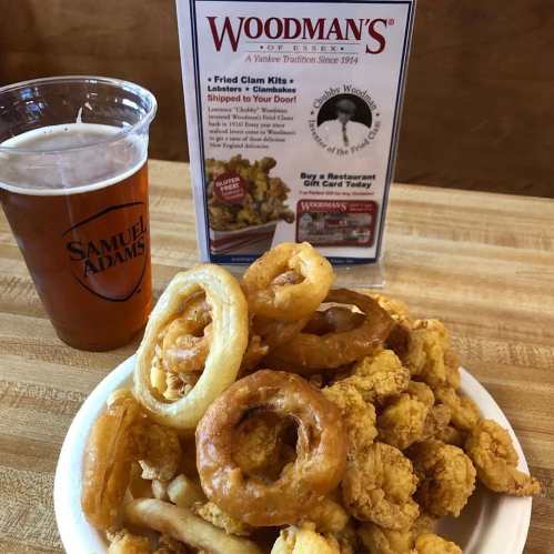 A plate of fried seafood, including clams and onion rings, next to a pint of beer and a menu at Woodman's of Essex.