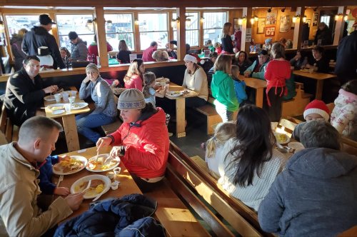 A busy restaurant filled with families and friends enjoying meals at wooden tables, with warm lighting and a cozy atmosphere.