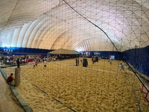 Indoor sand sports facility with a large inflatable dome, featuring players and spectators in a sandy area.