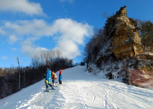 Skiers on a snowy slope with a rocky outcrop and blue sky in the background.