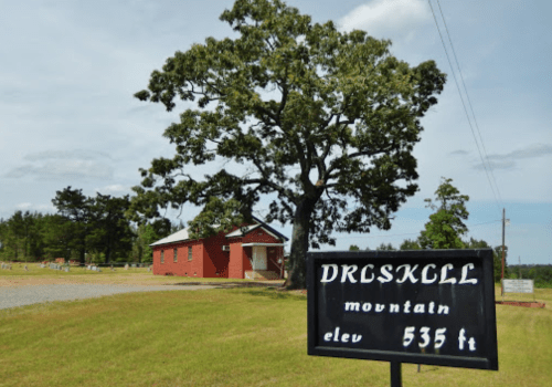 A red brick building beside a large tree, with a sign reading "DRLSKLL MOUNTAIN, elev 535 ft" in a grassy area.