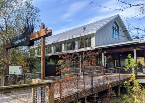 A modern building with large windows, surrounded by trees, featuring a sign that says "Y'all Come Back."