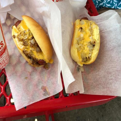 Two hot dogs on a red tray: one topped with cheese and onions, the other with cheese and chopped onions.
