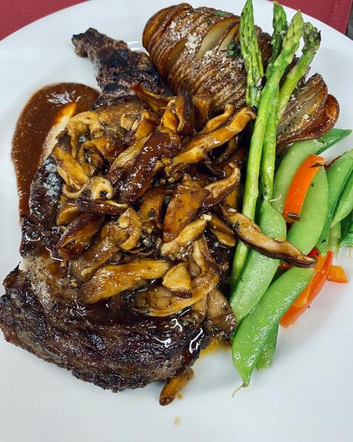 A plated meal featuring a grilled steak topped with mushrooms, asparagus, and colorful vegetables on the side.