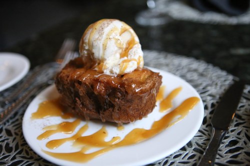 A warm dessert with a scoop of vanilla ice cream drizzled with caramel sauce on a white plate.