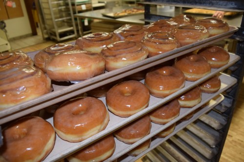 Freshly glazed donuts stacked on trays in a bakery, ready for sale.