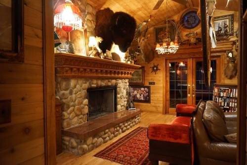 Cozy rustic living room with a stone fireplace, mounted animal heads, and wooden decor. Warm lighting enhances the ambiance.