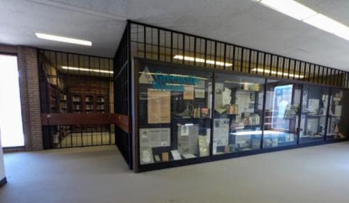 A glass display case in a library, showcasing historical documents and artifacts, with a gated entrance.
