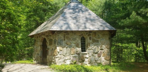 A small stone building with a conical roof, surrounded by lush green trees and foliage.