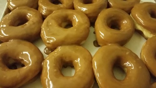 A close-up of a tray filled with glazed donuts, showcasing their shiny, caramel-colored icing.