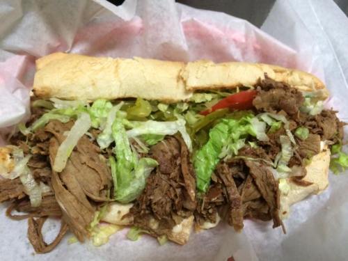 A hearty sandwich filled with shredded beef, lettuce, tomato, and pickles, served in a soft hoagie roll.