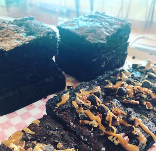 A close-up of stacked brownies topped with chocolate chips, nuts, and drizzled with caramel on a checkered paper.