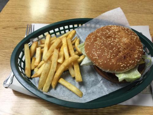 A sesame seed bun burger with lettuce, served with a side of golden French fries in a green basket.