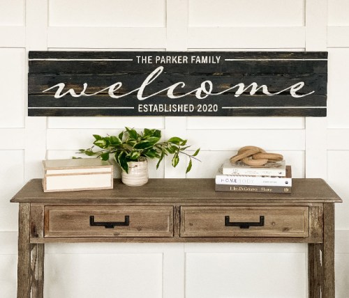 A wooden sign reading "The Parker Family welcome established 2020" above a rustic table with books and a plant.