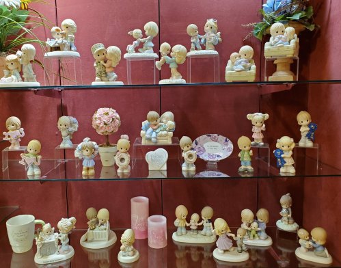 A display of various figurines depicting children in playful and affectionate poses on glass shelves.