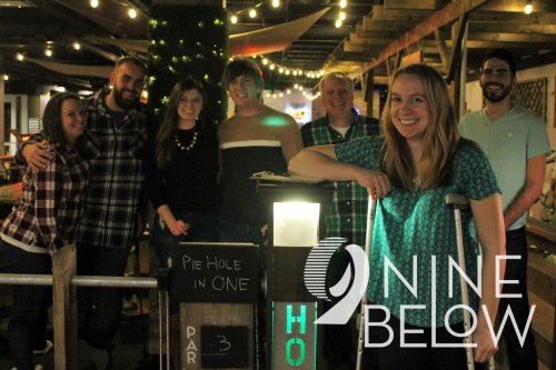 A group of friends poses together in a cozy venue, smiling and enjoying their time at Nine Below.
