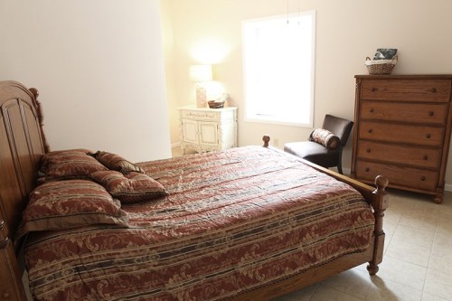 Cozy bedroom featuring a wooden bed, patterned bedding, a dresser, and a chair by a window.
