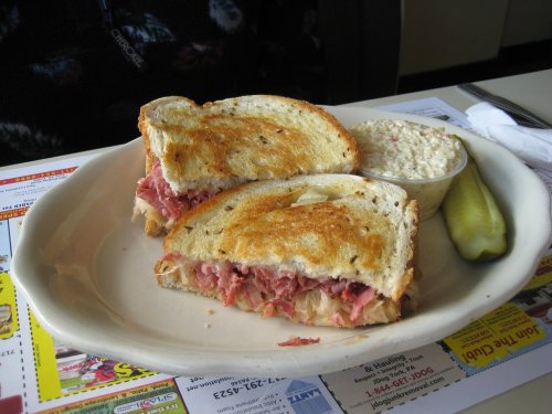 A toasted sandwich filled with meat and cheese, served with coleslaw and a pickle on the side.