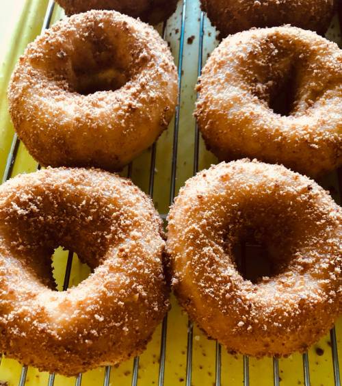 Four freshly made donuts coated in sugar, resting on a yellow cooling rack.