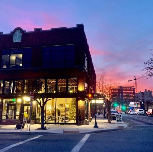 A corner building with large windows at sunset, featuring colorful skies and city lights in the background.