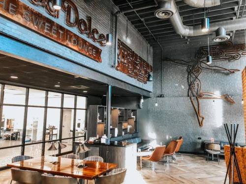 Modern lounge interior with wooden furniture, artistic wall decor, and large windows letting in natural light.