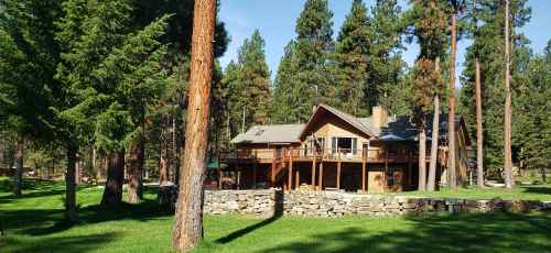 A wooden house surrounded by tall trees and a stone wall, set in a lush green landscape.