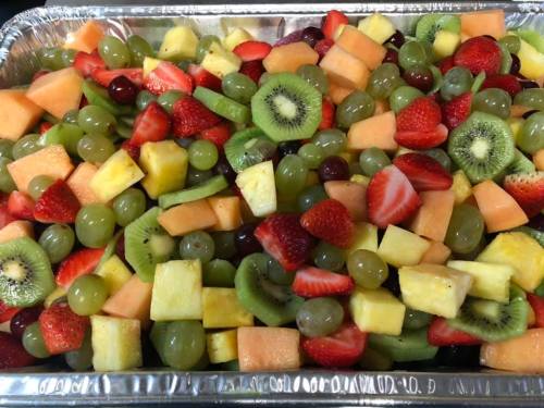 A colorful assortment of fresh fruit, including strawberries, grapes, kiwi, melon, and pineapple, in a large tray.
