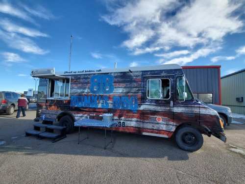 A colorful food truck named "Bunk's BBQ" parked outdoors with a blue sky and clouds in the background.