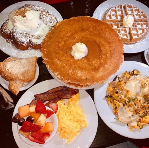 A delicious breakfast spread featuring pancakes, waffles, scrambled eggs, bacon, fruit, and toast on a table.