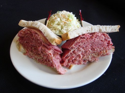 A plate featuring a large, sliced sandwich filled with corned beef, accompanied by a small bowl of coleslaw.