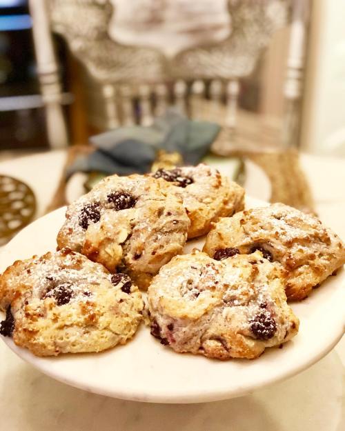 A plate of freshly baked scones dusted with powdered sugar, featuring bits of fruit, on a marble surface.