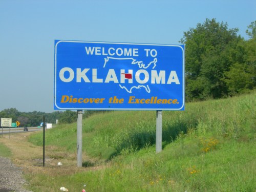 Blue welcome sign for Oklahoma with the text "Discover the Excellence" and a map outline of the state.
