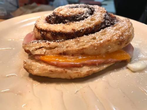 A spiral pastry with ham and cheese, dusted with powdered sugar, on a plate.