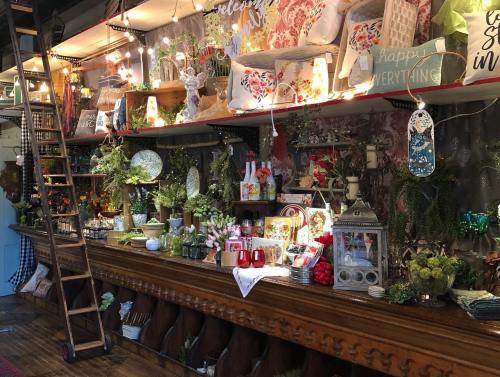 A cozy shop display featuring decorative items, plants, and colorful pillows on wooden shelves with warm lighting.