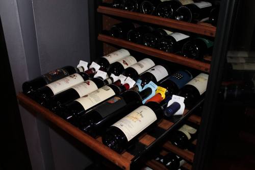 A wooden wine rack filled with various bottles of wine, some labeled, in a dimly lit storage area.
