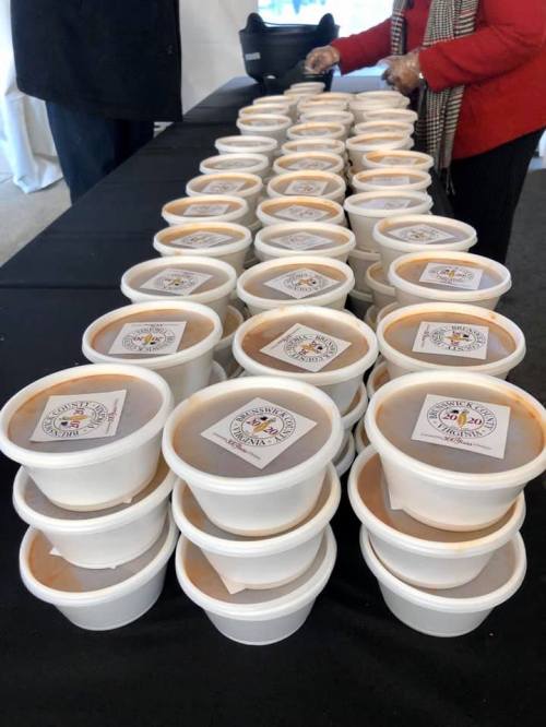 A table lined with stacked cups of food, each labeled with a logo, and a person in a red jacket nearby.
