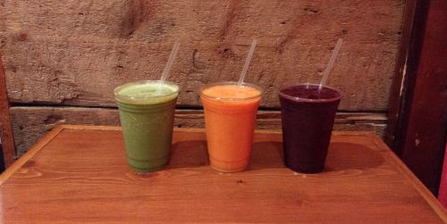 Three colorful smoothies in clear cups sit on a wooden table against a rustic background.
