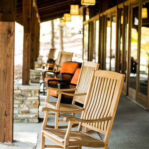 A row of wooden rocking chairs on a porch, with warm lighting and a natural setting in the background.