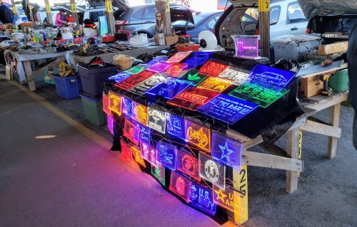 A vibrant display of neon signs on a table at a market, surrounded by various items for sale.