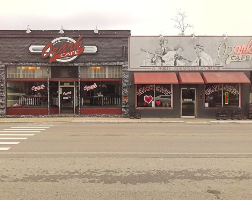 Two adjacent buildings featuring Ozark Café signage, one modern and the other with a vintage design, on a street.