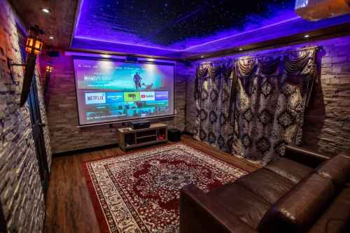 Cozy home theater with a large screen, plush seating, decorative curtains, and ambient purple lighting.