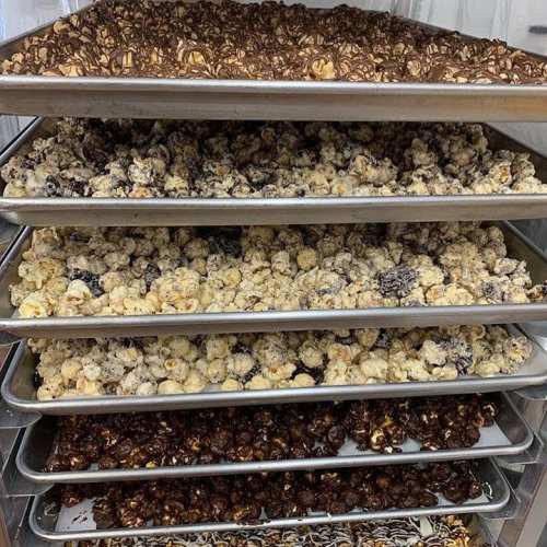 Trays of assorted popcorn varieties, including chocolate-covered, caramel, and drizzled flavors, stacked neatly.