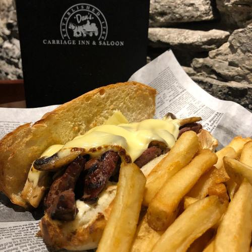 A hearty sandwich with steak, mushrooms, and melted cheese, served with a side of golden fries.