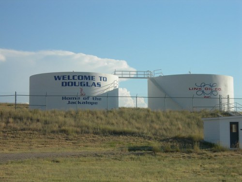 Two large oil tanks with "Welcome to Douglas" and "Home of the Jackalope" painted on them, set against a blue sky.