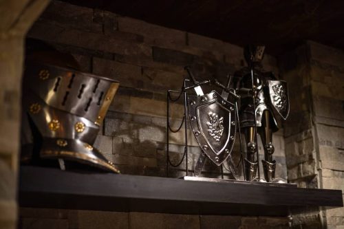 A display of medieval armor, including a helmet and knight figurine with shields, set against a stone wall.