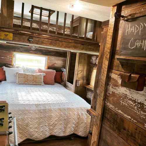 Cozy rustic bedroom with a lofted bed, wooden walls, and warm lighting, featuring a white quilt and decorative pillows.
