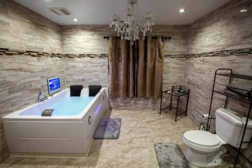 Modern bathroom featuring a bathtub, chandelier, decorative curtains, and stylish tile walls.