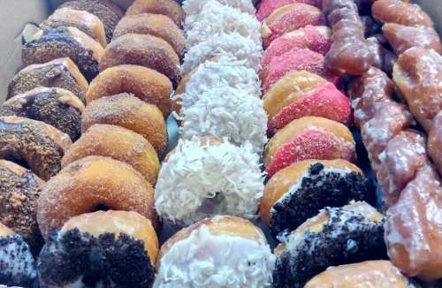 A variety of colorful donuts arranged in a box, including glazed, coconut, and chocolate-covered options.